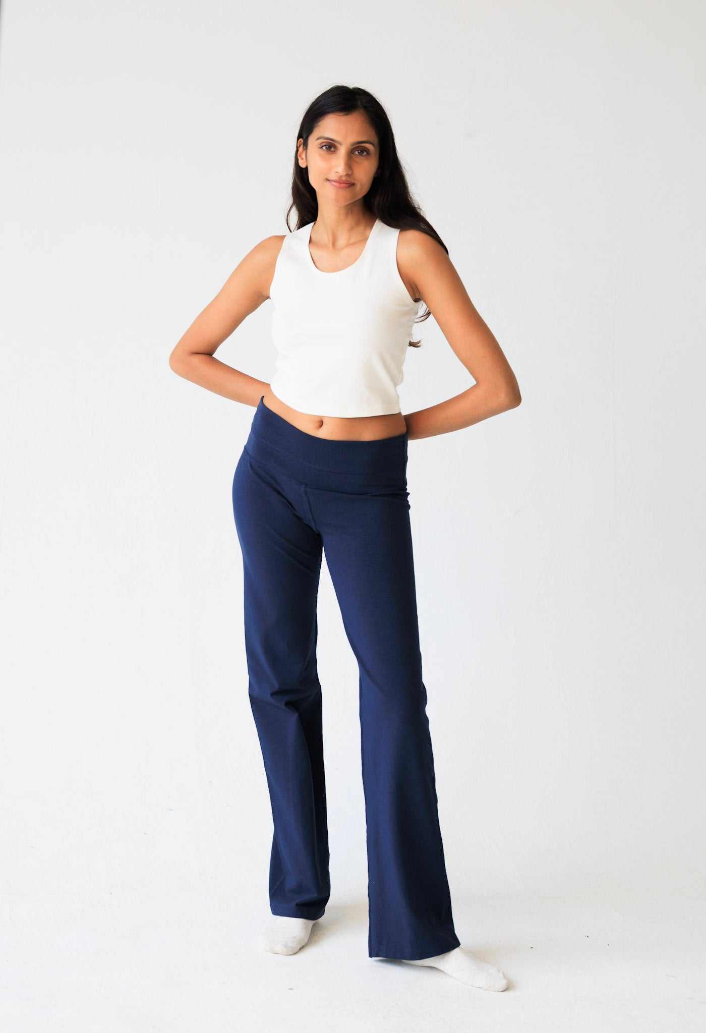 Woman wearing a white sleeveless top and blue flared pants on a white background