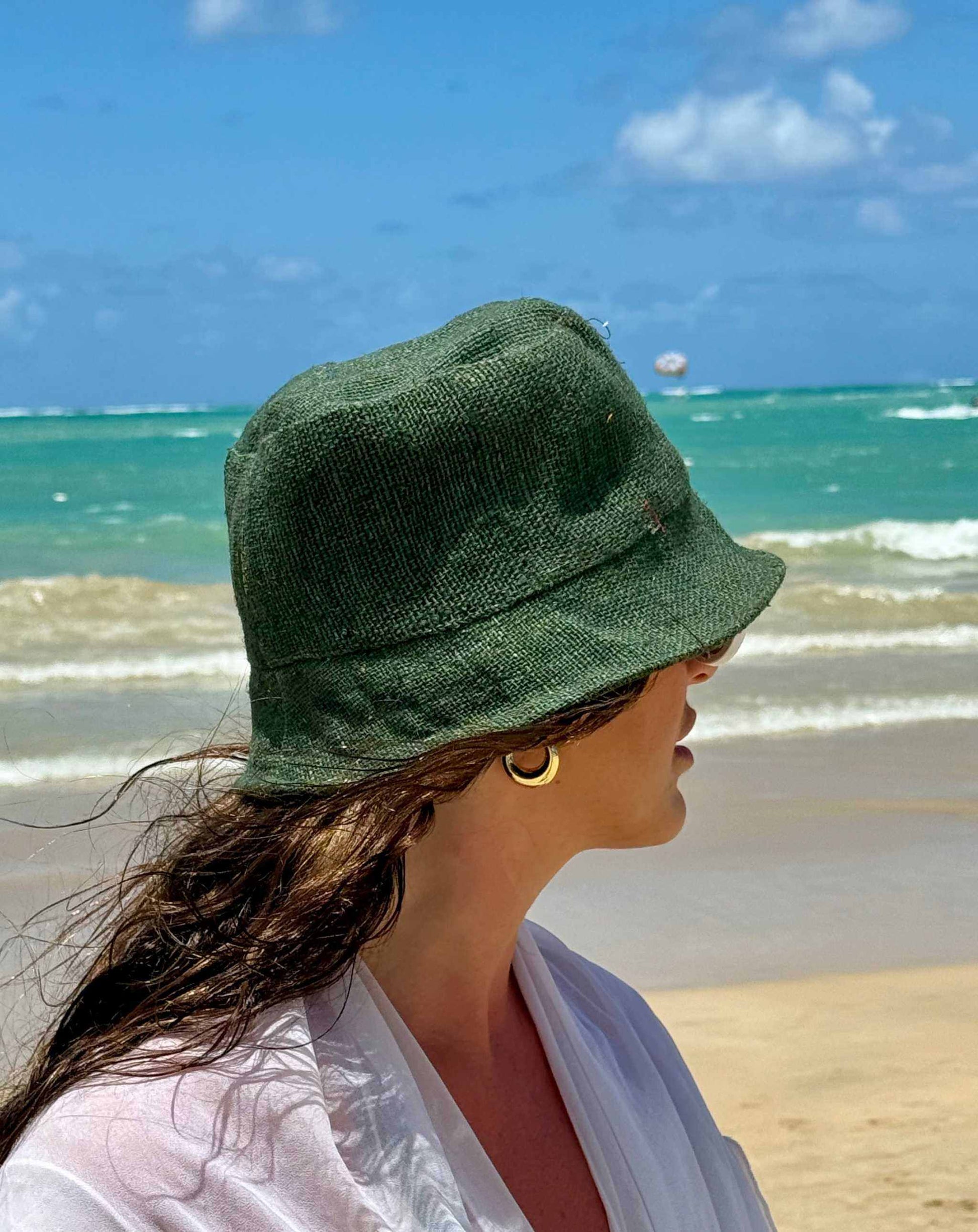Green hemp bucket hat on person at the beach, featuring sustainable materials and stylish design.