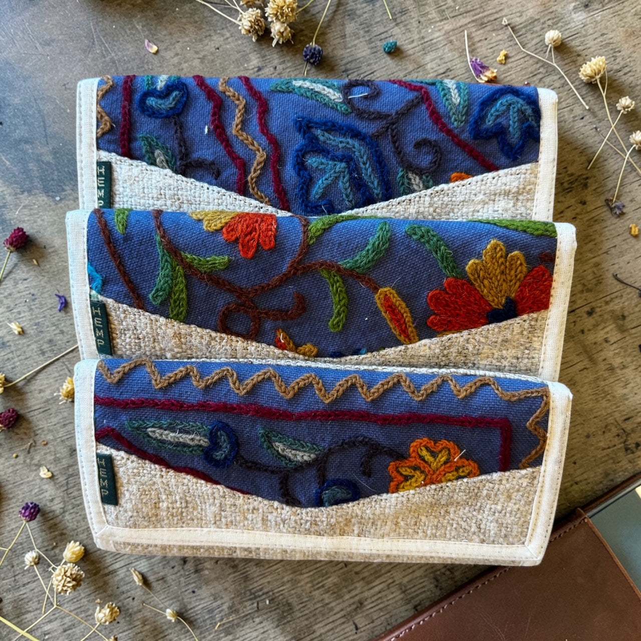 Handmade tri-fold hemp wallet with floral embroidery, sustainable vegan material, and multiple compartments for cards and cash.
