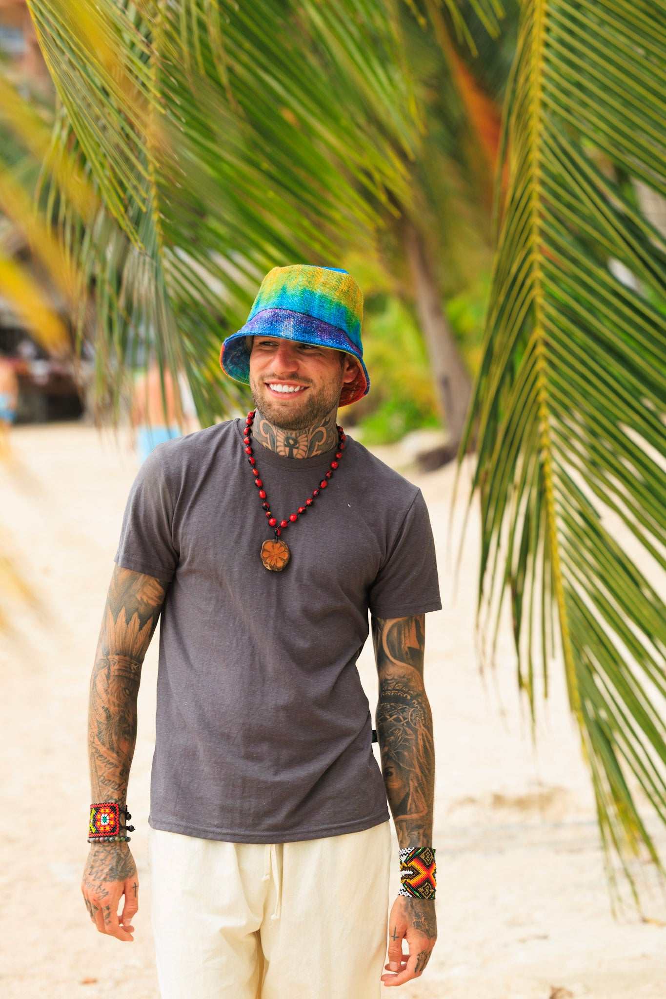Man wearing a colorful bucket hat and gray t-shirt standing in front of palm trees.