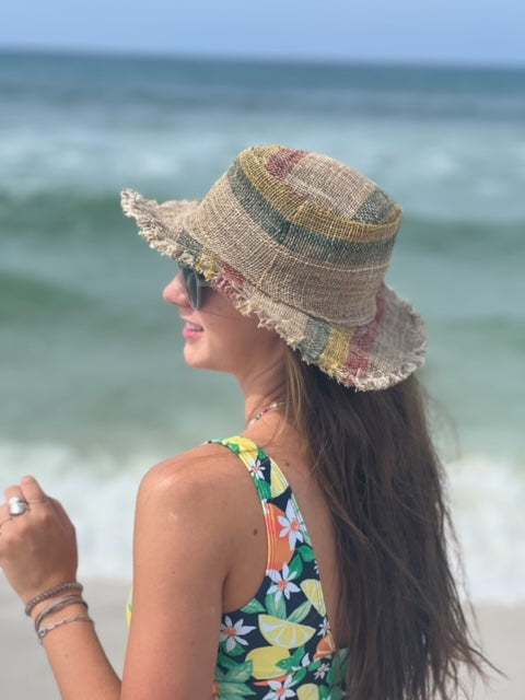 Woman wearing a colorful straw hat and floral swimsuit on a beach.