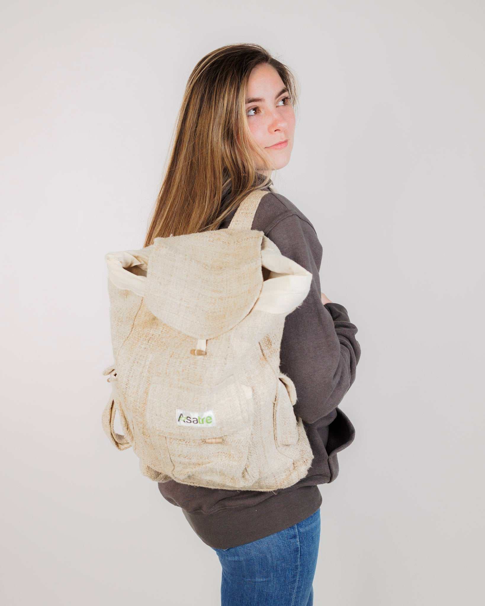 Woman wearing a beige hemp bag backpack against a plain background