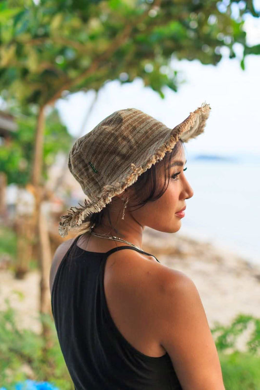 Woman wearing a sage striped hemp linen sun hat with a frayed brim at the beach.