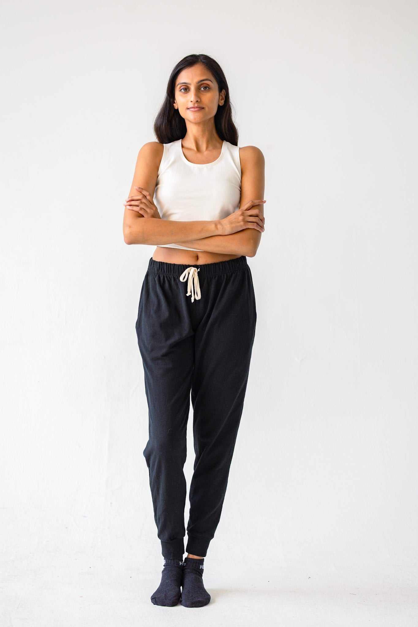 Woman wearing a white tank top and black pants with a white background