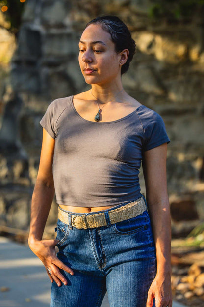 Woman wearing a gray top and blue jeans standing outdoors with a stone wall background