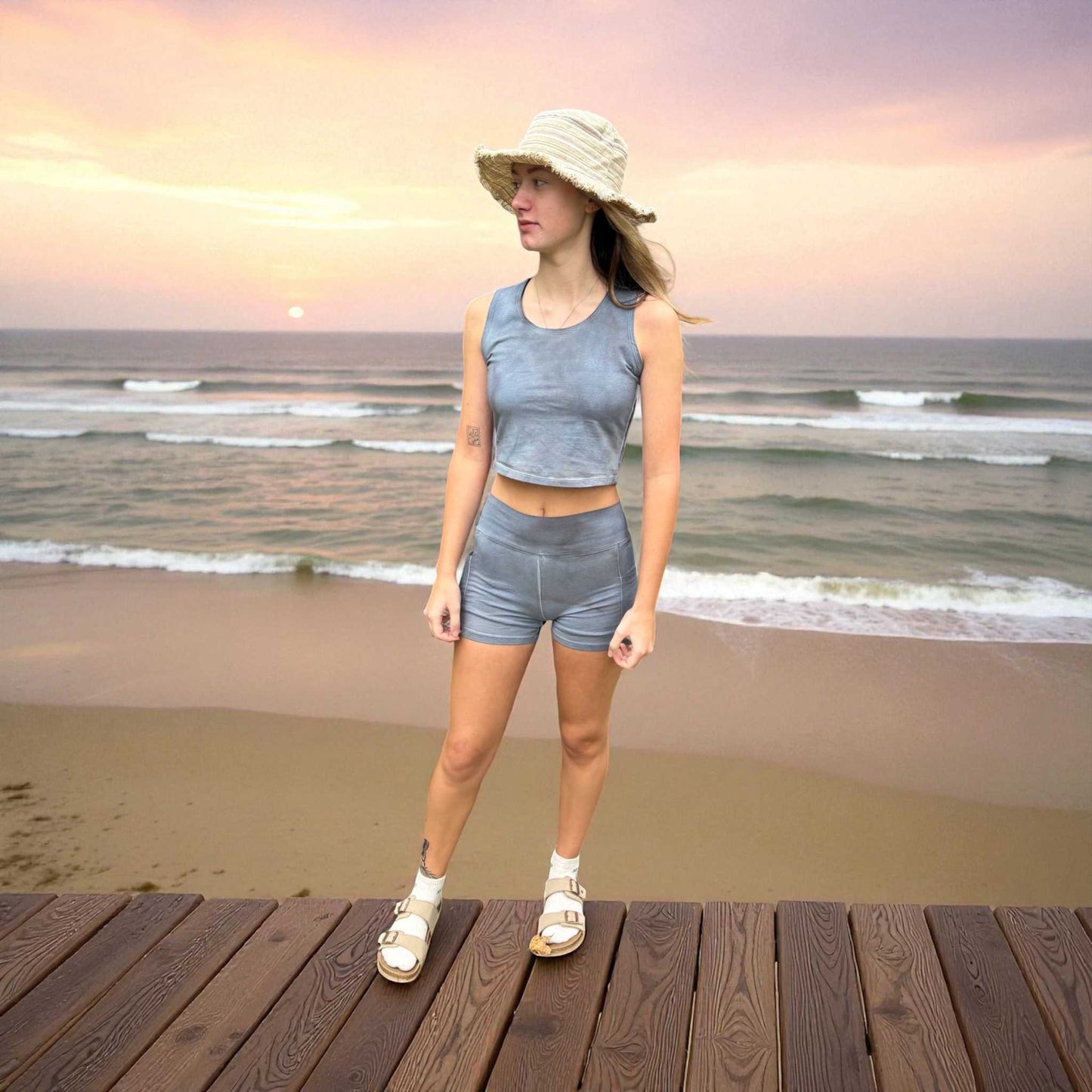Woman standing on a wooden boardwalk at the beach during sunset.