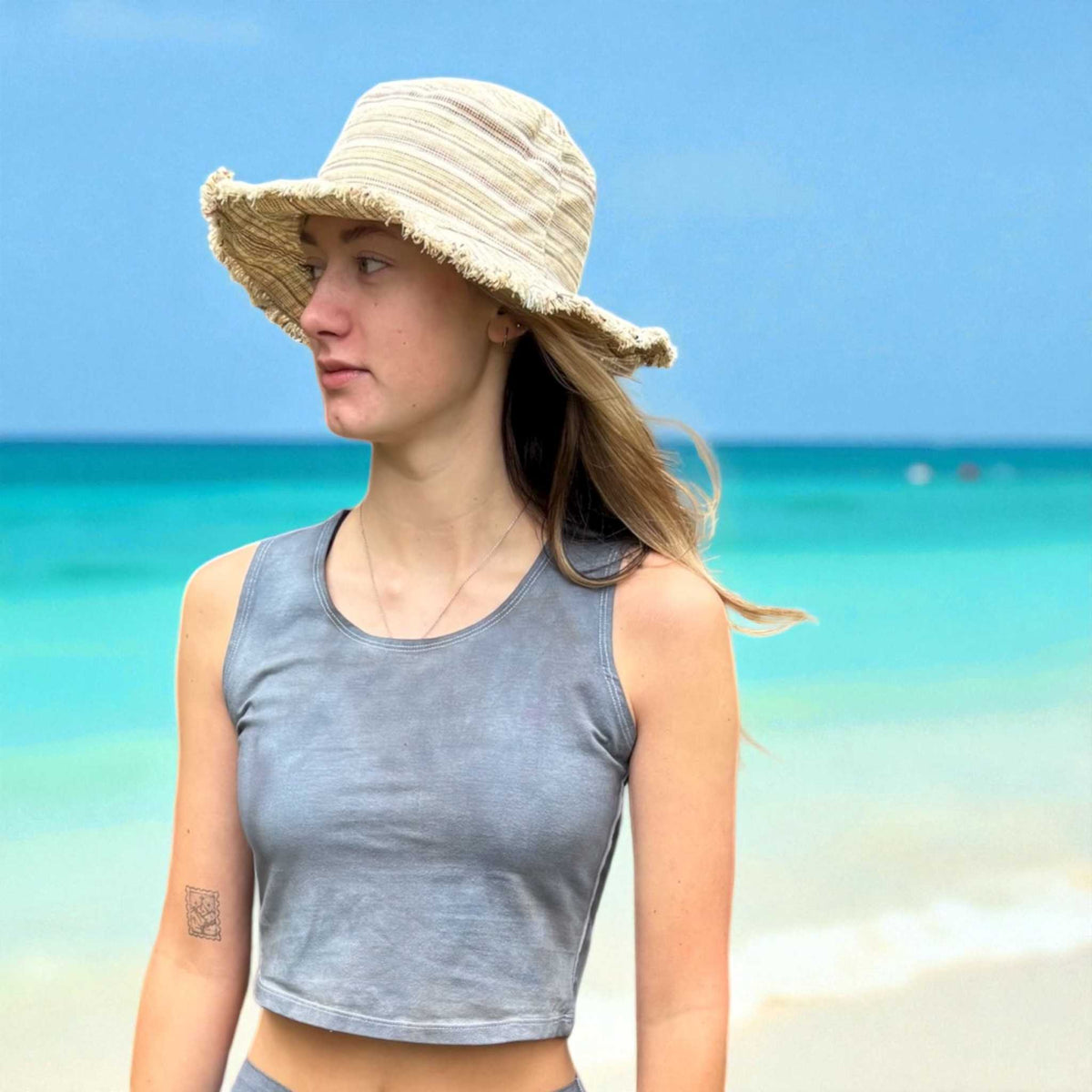 Woman wearing a straw hat on a beach with clear blue water and sky.