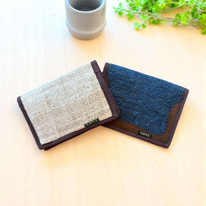 Two fabric wallets, one gray and one blue, on a light surface with a plant in the background.