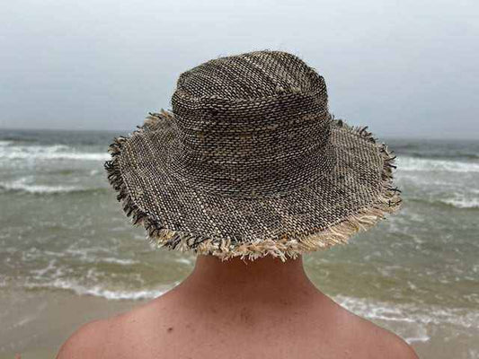 Back view of a wide brim hemp sun hat worn at the beach, showcasing its natural woven texture and frayed edges.